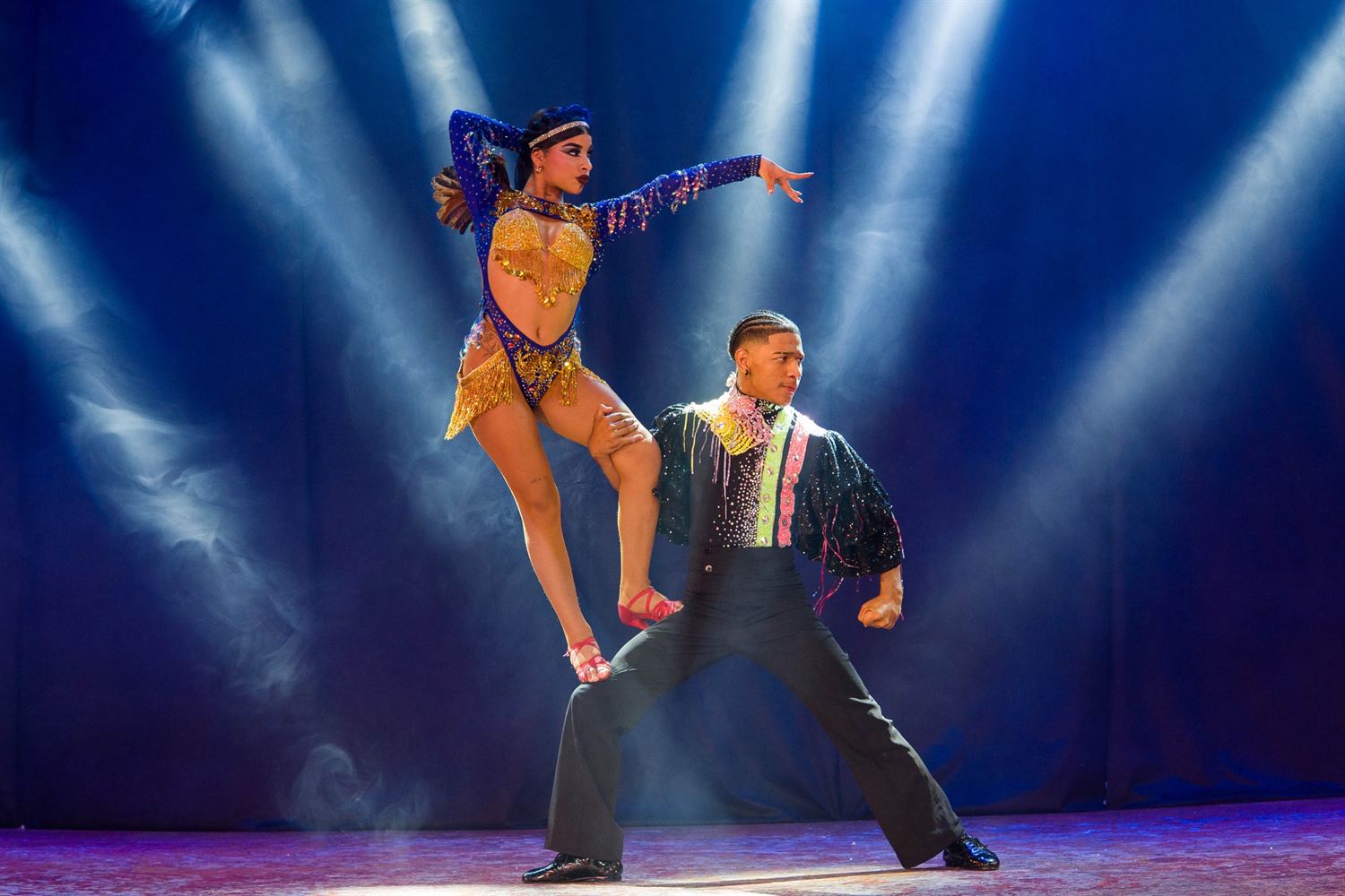 A dancer in blue and gold poised on her partner's thigh